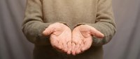 Woman in beige sweater with open cupped hands in receiving gesture against neutral background for charity, giving, support and help concepts.