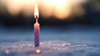 Single lit striped birthday candle glowing on sparkling snow surface against blurred winter sunset background, creating magical festive atmosphere.