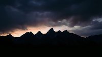 Dramatic mountain silhouettes against stormy sunset sky with golden and purple clouds, moody atmospheric landscape for nature and travel projects.