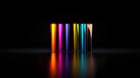 Colorful metallic cylinders standing in row casting vibrant reflections on dark glossy surface. Minimalist composition with gradient lighting effects creates modern design appeal.