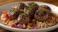 Savory meatballs with fresh herbs served over seasoned rice with tomato sauce and vegetables on white plate for restaurant menu and recipe content.