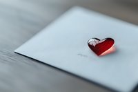 Red glass heart on white envelope creates romantic mood with soft blur background, suitable for Valentine's Day cards, wedding invitations and love messages.