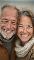 Happy mature Caucasian couple smiling together outdoors, senior man with gray beard and woman in cozy sweaters showing genuine joy and love in golden light.