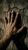 Male hand with visible veins and skin texture pressed against cracked concrete wall surface, casting dramatic shadow. Suitable for concepts of struggle, resilience, hardship, construction, labor, and emotional distress.