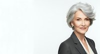 Mature woman with gray hair wearing black blazer and white shirt against white background, professional headshot for business, corporate, and executive use.