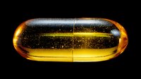 Transparent golden capsule pill with visible particles inside on black background, used in pharmaceutical advertising and health concepts.