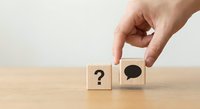 Hand placing wooden cube with speech bubble next to question mark block on desk for communication and inquiry concepts.