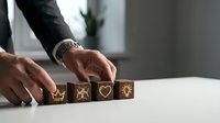 Close-up of male hands arranging wooden blocks with gold symbols including crown, star, and heart on white surface for business success and growth concept.