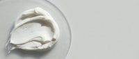 Creamy white whipped cream or sour cream dollop on transparent glass plate against neutral background, suitable for food styling and culinary content.