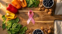 Pink ribbon surrounded by healthy foods including colorful bell peppers, leafy greens, blueberries and walnuts on rustic wooden cutting board for awareness.