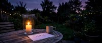 Candlelit outdoor table at dusk with a sorry note and mug, evoking apology, forgiveness, and heartfelt emotion in a garden setting.