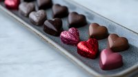 Heart-shaped chocolate candies and wrapped bonbons in pink and red foil arranged on gray ceramic plate, romantic confectionery composition on marble background.
