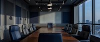 Modern corporate boardroom with large wooden conference table and leather chairs overlooking city skyline through floor-to-ceiling windows.