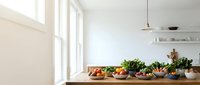 Modern kitchen counter with fresh vegetables and wooden bowls in bright minimalist interior with white walls and natural lighting for healthy cooking.