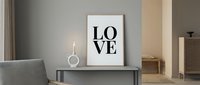Minimalist interior with framed LOVE typography poster on console table, candle, and neutral decor for modern home styling inspiration.