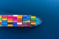 Aerial view of colorful cargo containers stacked on freight ship bow moving through deep blue ocean waters, minimalist composition for logistics and shipping concepts.