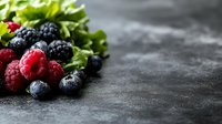 Fresh mixed berries with raspberries, blackberries and blueberries on dark stone background with green lettuce leaves and copy space for text.