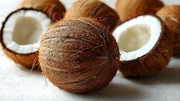 Fresh whole and halved coconuts showing white flesh inside, arranged on light surface with natural shadows, macro food photography for healthy eating concept.