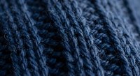 Navy blue knitted wool fabric with cable pattern texture close-up macro shot for fashion design and textile industry backgrounds.