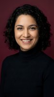 Professional Middle Eastern woman with curly hair smiling confidently in black turtleneck against burgundy background for business and corporate use.