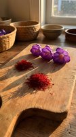 Dried saffron threads and purple crocus flowers on a rustic wooden cutting board in warm sunlight, with wicker basket and bowls in background.