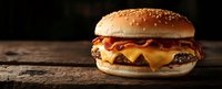 Juicy cheeseburger with melted cheese, bacon and sauce on rustic wooden background, dark moody food photography with copy space for menu design.