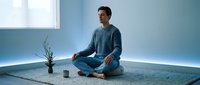 Young Caucasian man in comfortable clothing practicing mindfulness meditation in modern minimalist room with soft natural lighting and zen decor.