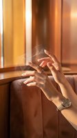 Hands holding transparent smartphone with warm sunlight streaming through window creating golden hour atmosphere in modern interior space.