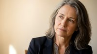 Middle-aged woman with long gray hair and fair complexion wearing dark blazer, professional headshot against neutral background for corporate or business use.
