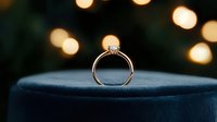 Diamond engagement ring on dark velvet surface with soft golden bokeh lights creating romantic atmosphere, luxury jewelry photography for wedding proposals.