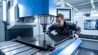 Professional male engineer operating CNC milling machine in modern manufacturing facility. Industrial worker monitoring automated production process.