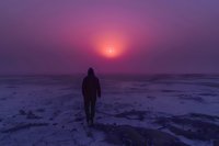 Silhouette of person walking on snowy landscape at sunset with vibrant purple and pink sky, creating atmospheric winter scene.