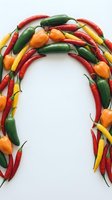 Colorful hot chili peppers arranged in arch shape on white background, featuring red, green, yellow and orange varieties for cooking and culinary design projects.