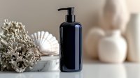 Black cosmetic pump bottle with seashells and coral on marble surface against neutral beige background, mockup for beauty product packaging and branding.