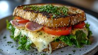 Fresh deli sandwich on toasted sesame bread with melted cheese, crisp lettuce, ripe tomatoes, red onions and herbs served on ceramic plate, close-up view.