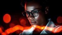 Young African American woman in glasses illuminated by dramatic red neon lights against dark background with bokeh effect, creating modern urban nighttime portrait.