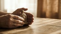 Hands protecting house keys on wooden table in warm sunlight, symbolizing home security, real estate investment and property protection concept.