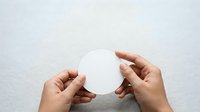 Hands holding blank white circle on neutral background for branding, mockup, and design projects.
