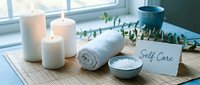 Serene self care spa setup with lit candles, rolled towel, sea salt bowl, and eucalyptus on bamboo mat near bright window.