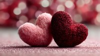 Two textured fabric hearts in pink and burgundy red colors with romantic bokeh background for Valentine's Day cards and love-themed designs.
