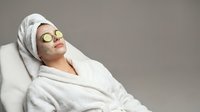 Young woman relaxing in white bathrobe with cucumber eye mask during spa treatment. Self-care wellness routine for skincare and beauty therapy session.