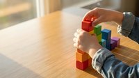 Child hands building colorful wooden block tower on table, early childhood development and creative play activity for learning motor skills.