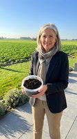 Mature Caucasian businesswoman holding bowl of rich dark soil in agricultural field showcasing sustainable farming and organic agriculture practices.