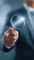 Business professional holding magnifying glass showing growing bar chart graph, symbolizing market analysis and financial growth performance monitoring.