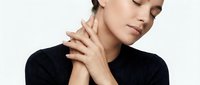 Young Caucasian woman in black turtleneck gently touching her neck with eyes closed, expressing relaxation and skincare wellness.