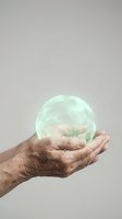 Elderly hands holding glowing green energy sphere representing healing, protection, and spiritual power against neutral background.