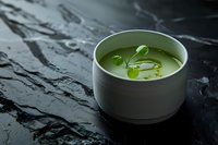 Green pea soup garnished with microgreens in white ceramic bowl on dark stone background with water drops, moody restaurant food styling.