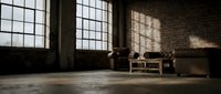 Empty industrial loft interior with large windows casting dramatic shadows on brick walls and concrete floor, vintage furniture creating moody atmosphere.