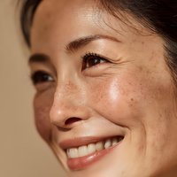 Close-up portrait of smiling young Asian woman with natural freckles and glowing skin showing authentic beauty and confidence for skincare campaigns.
