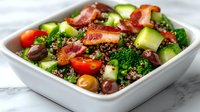 Fresh quinoa salad with crispy bacon, cucumber, cherry tomatoes and mixed greens in white bowl. Healthy protein-rich meal for lunch or dinner menu.